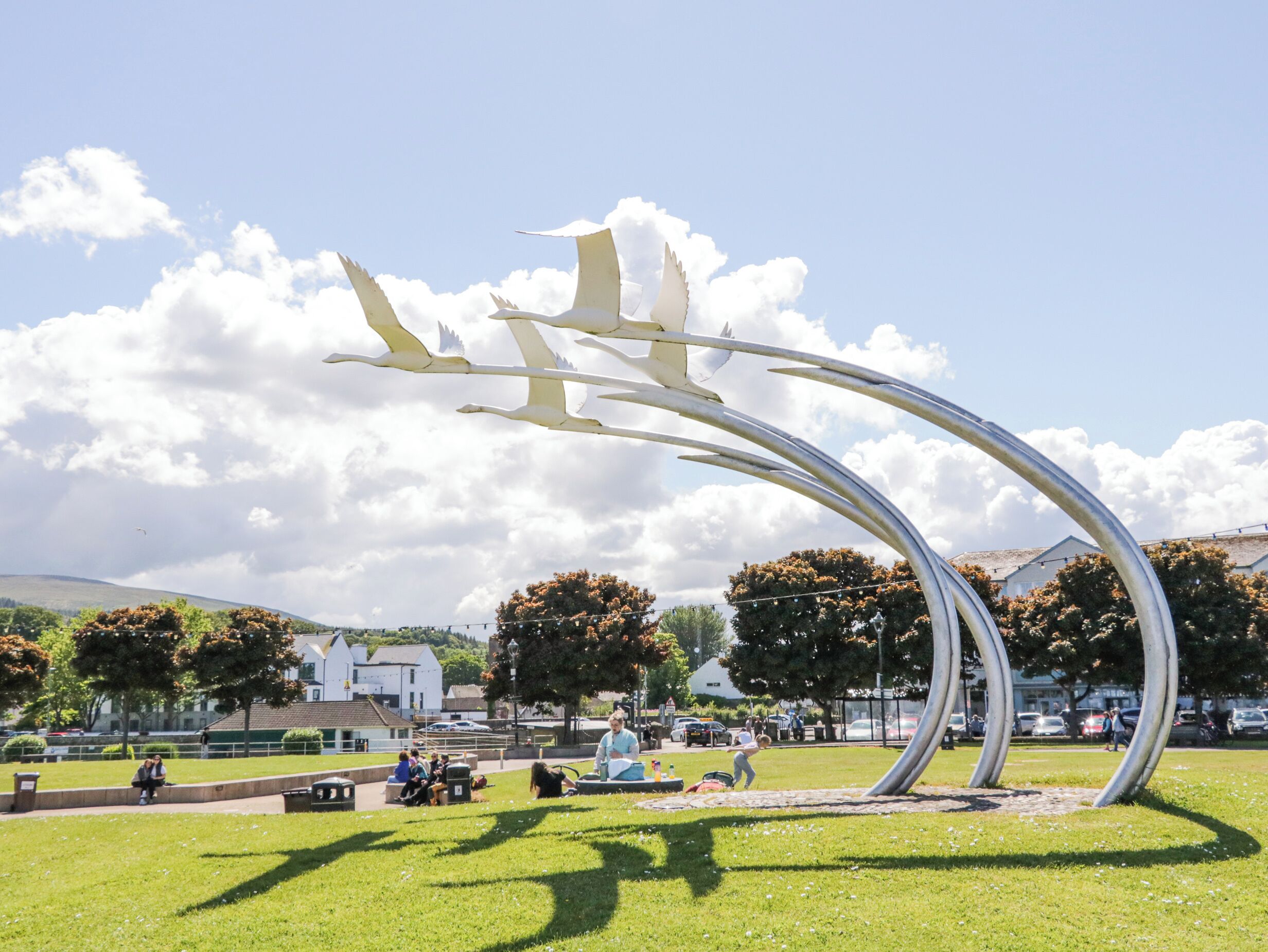 Un parque con una gran escultura metálica, zonas de césped y árboles.
