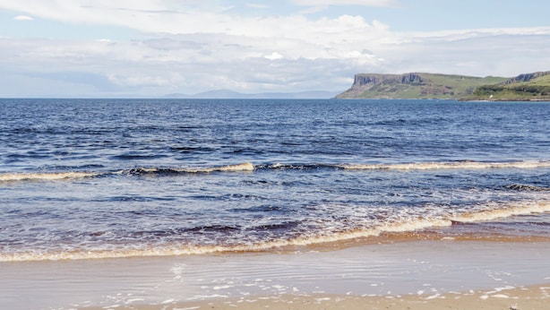 Une plage avec des vagues, un ciel dégagé et des falaises lointaines.