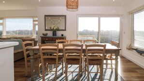 A dining area with a wooden table and chairs, a rug, and a large window with a view. - Awel-y-mor (Holyhead)