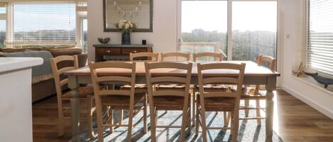 A dining area with a wooden table and chairs, a rug, and a large window with a view.