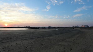 A beach with a sunset, sandy shore, and distant buildings. - Awel-y-mor (Holyhead)