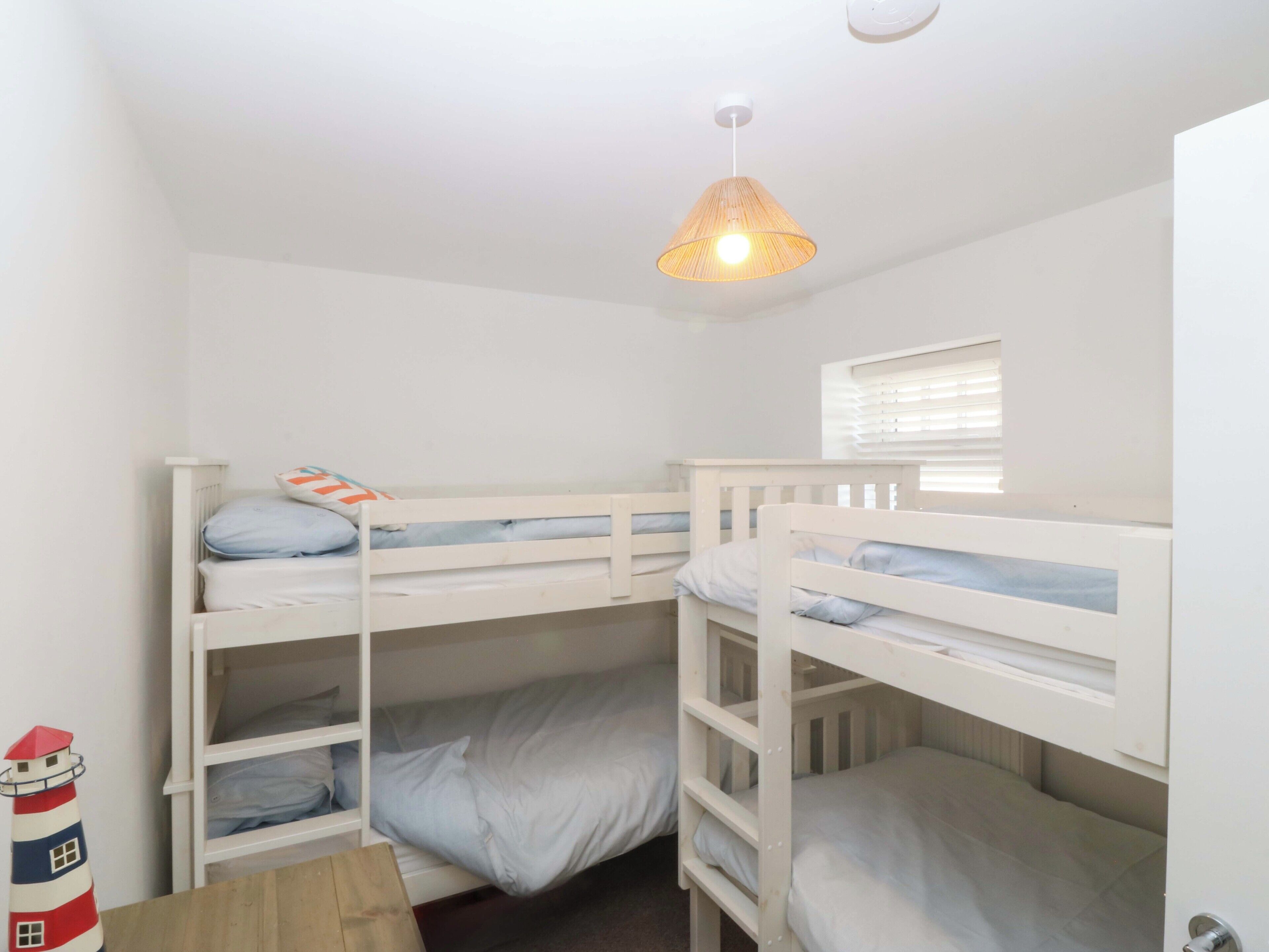 A room with three bunk beds, a small window with blinds, and a hanging light fixture.