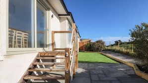 A wooden staircase leading to a house with a stone patio and a small lawn. - Awel-y-mor (Holyhead)