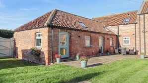 A brick house with a tiled roof, a front door, and a small porch area with potted plants. - The Old Stable (Hull)