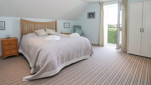 A bedroom with a large bed, a wooden nightstand, a wardrobe, and a balcony with a view. - The Old Stable (Hull)