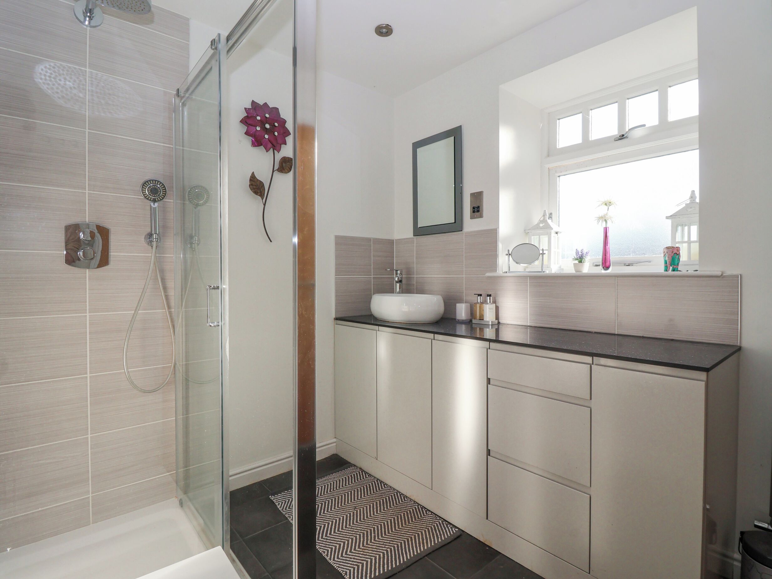 A modern bathroom with a glass shower enclosure, a white sink, and a window with a view.