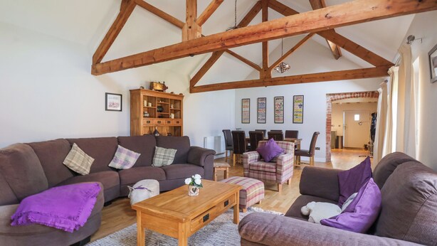 A spacious living room with high wooden beams, a brown sofa set, a wooden coffee table, and a plaid armchair. - The Old Stable (Hull)
