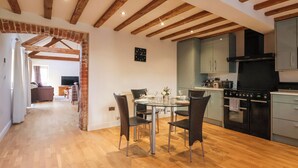 A spacious kitchen with modern appliances, a dining area with a glass table and chairs, and exposed wooden beams on the ceiling. - The Old Stable (Hull)