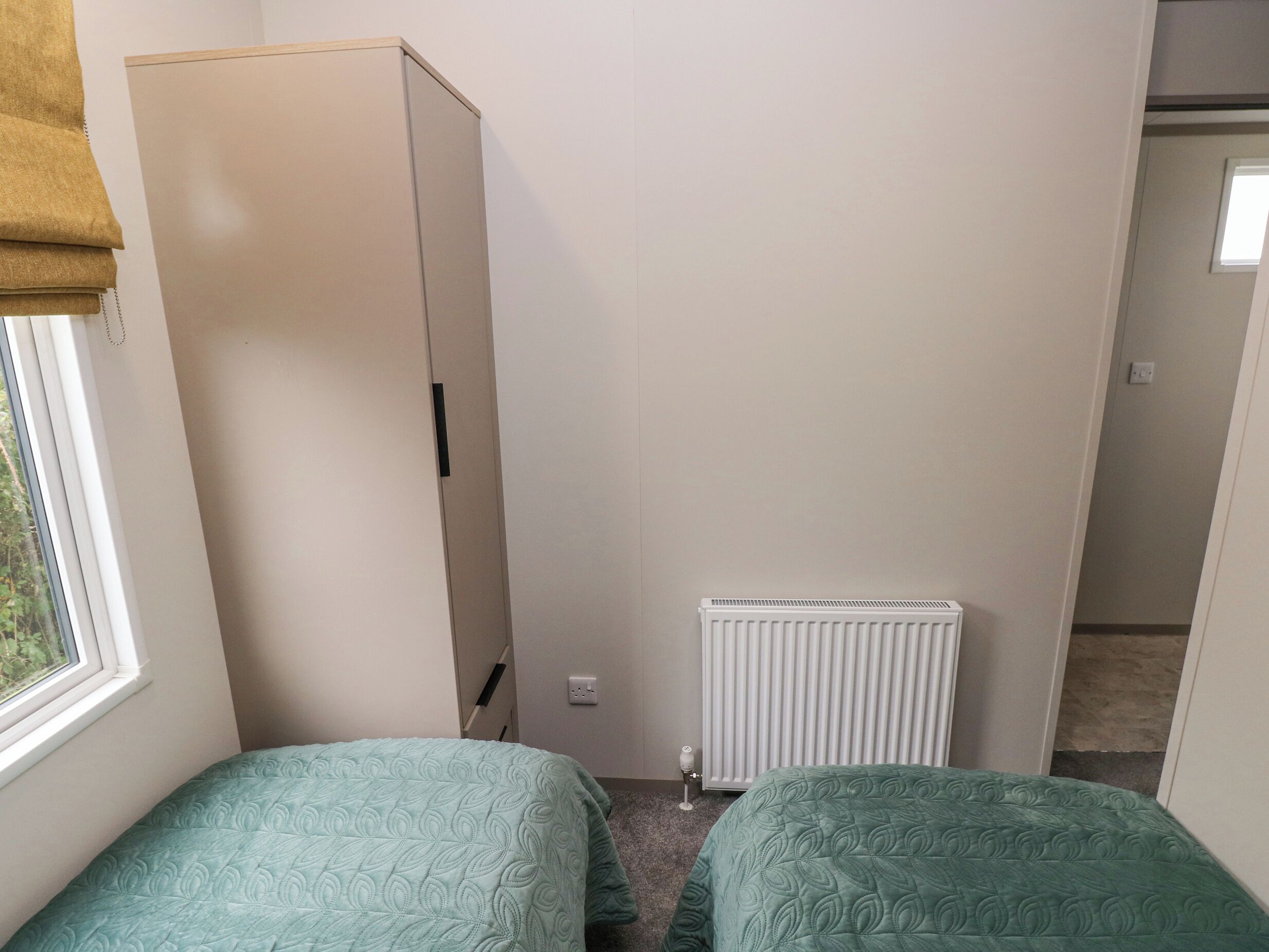 Une petite pièce, peu meublée, avec deux lits simples, un radiateur et une armoire.