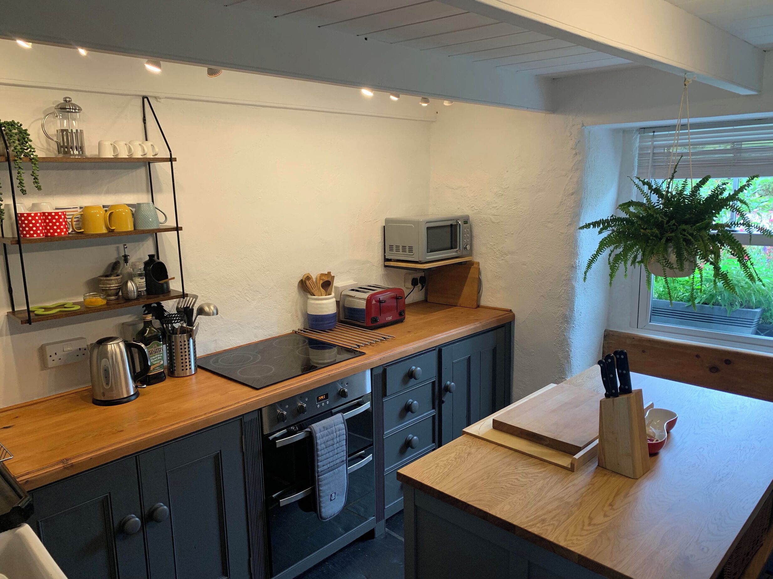 A compact kitchen with a wooden countertop, built-in oven, and a microwave on a shelf.