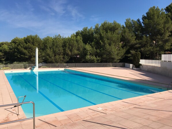A rectangular swimming pool with clear blue water, surrounded by a tiled deck and a white fence.