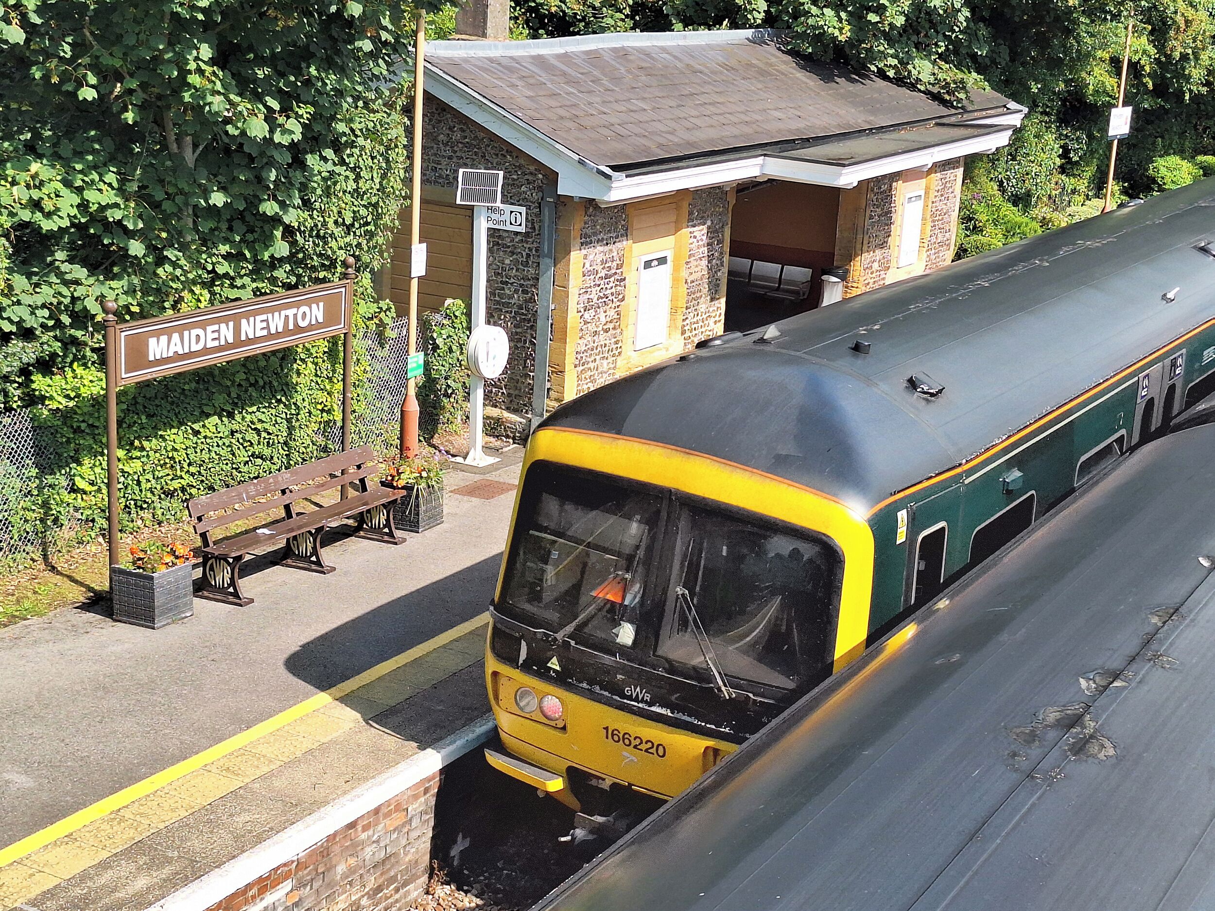 A train station platform with a bench and a sign reading "Maiden Newton".