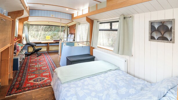 A cozy RV bedroom with a bed, a desk, and a window with curtains. - Walter (Wells-next-the-Sea)