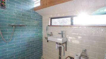 A bathroom with a blue-tiled shower wall, a white sink, and a window above the sink.