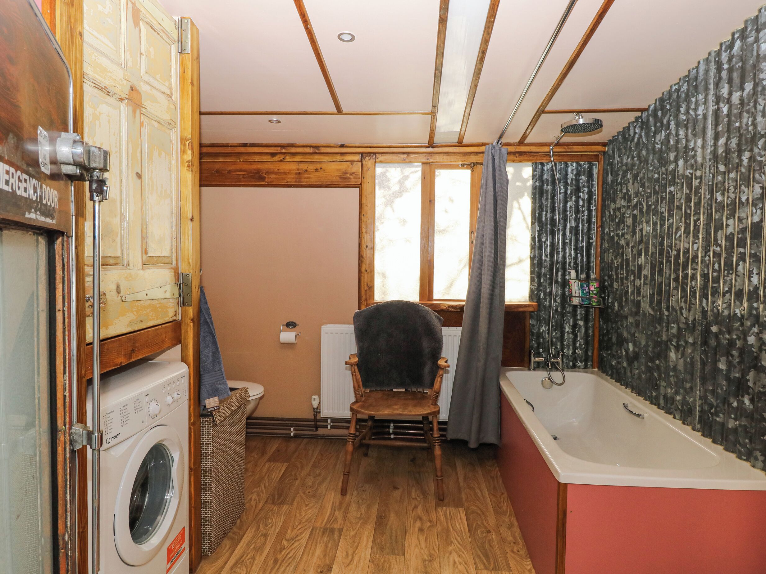 Een kleine badkamer met een wasmachine, een houten stoel, een badkuip en een radiator.