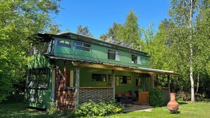 A green two-story house with a porch, surrounded by trees and grass. - Walter (Wells-next-the-Sea)
