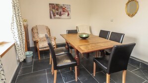 A dining area with a wooden table, black chairs, a floral armchair, and a painting on the wall. - Ty Siabod (Betws-Y-Coed)