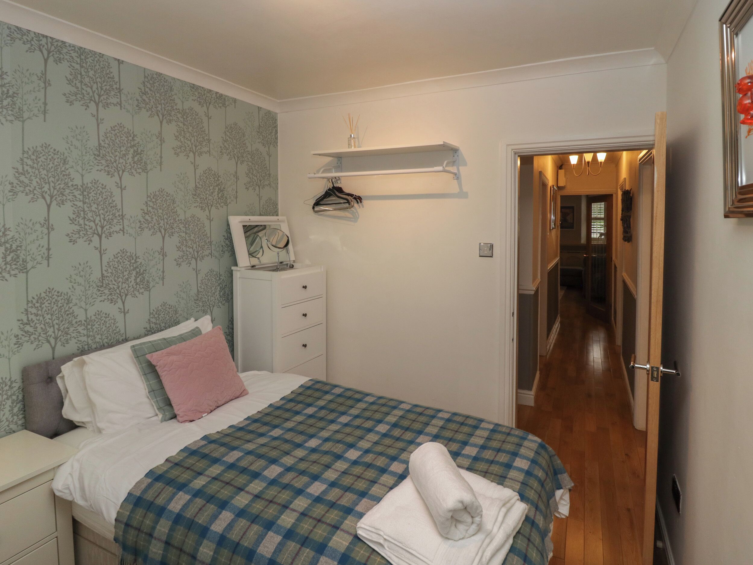 A bedroom with a bed, a nightstand, a dresser, a mirror, and a hallway leading to another room.