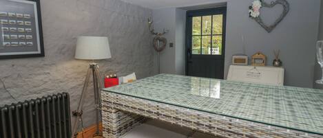 Eine moderne Küche mit Esstisch aus Glas, Korbmöbeln, einer Heizung und einem gerahmten Bild an der Wand.