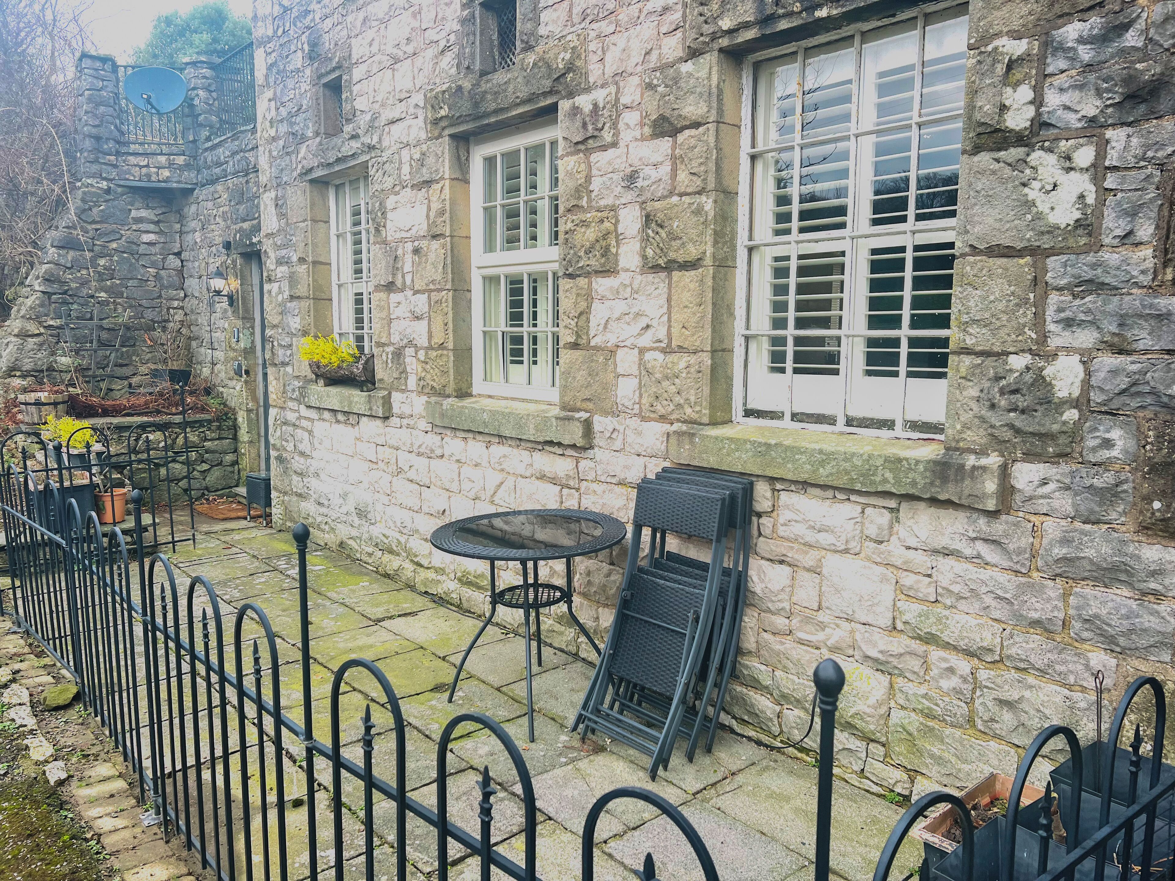 Un edificio de piedra con dos ventanas y un pequeño espacio al aire libre con una mesa y sillas.