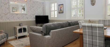 A cozy living room with a grey sofa, a television, and a wooden dining table.