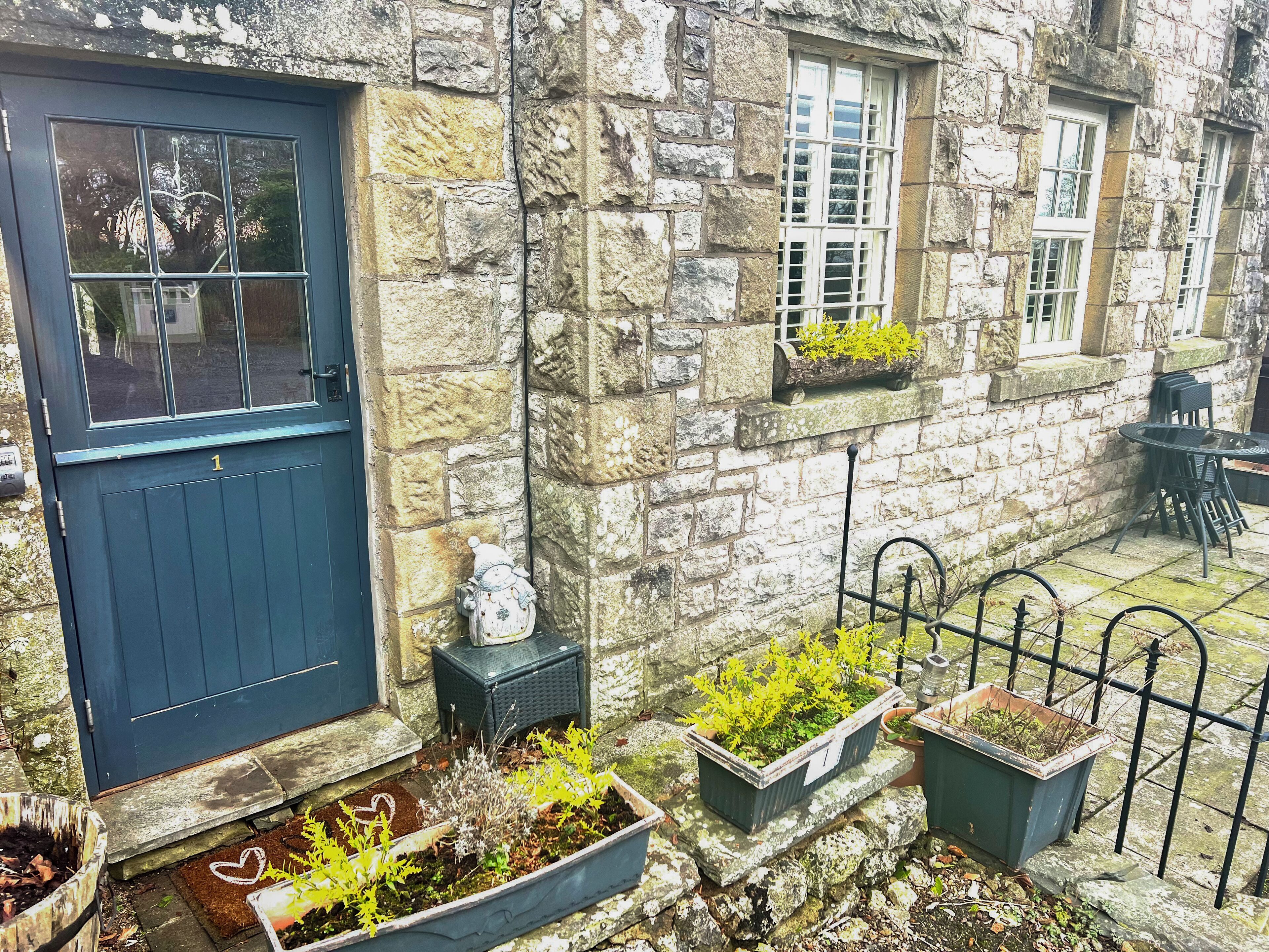 A stone building with a dark blue door, potted plants, and a metal fence.