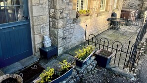 A stone building with a blue door, a small garden area with potted plants, and a metal fence. - 1 Boarbank Farm (Grange-over-Sands)
