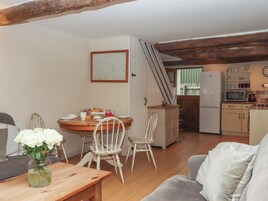 A cozy living room with a dining area, wooden floors, a kitchen with a refrigerator and microwave, and a staircase leading to an upper level.