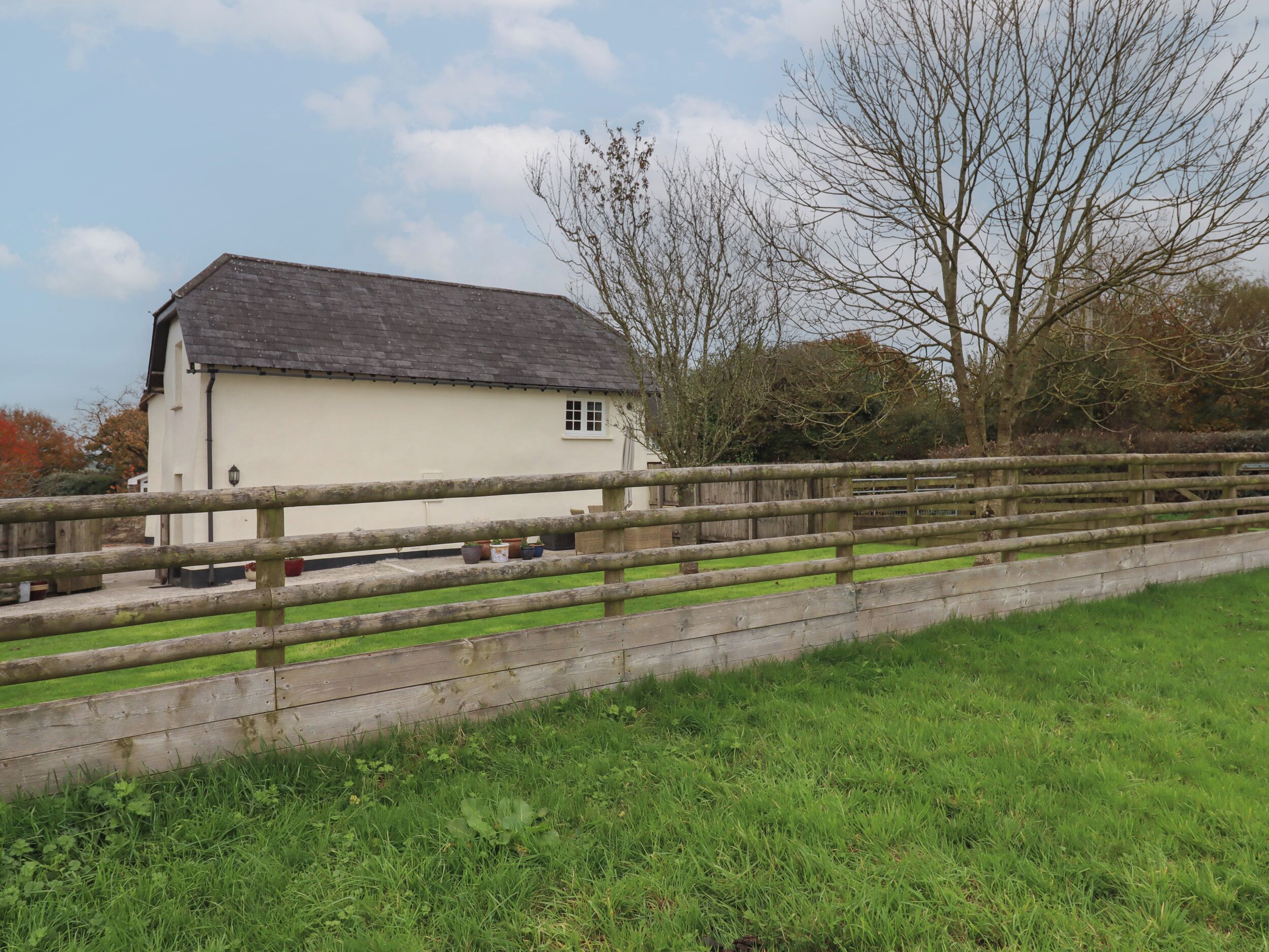 A white building with a sloped roof, a wooden fence, and a grassy area in front.