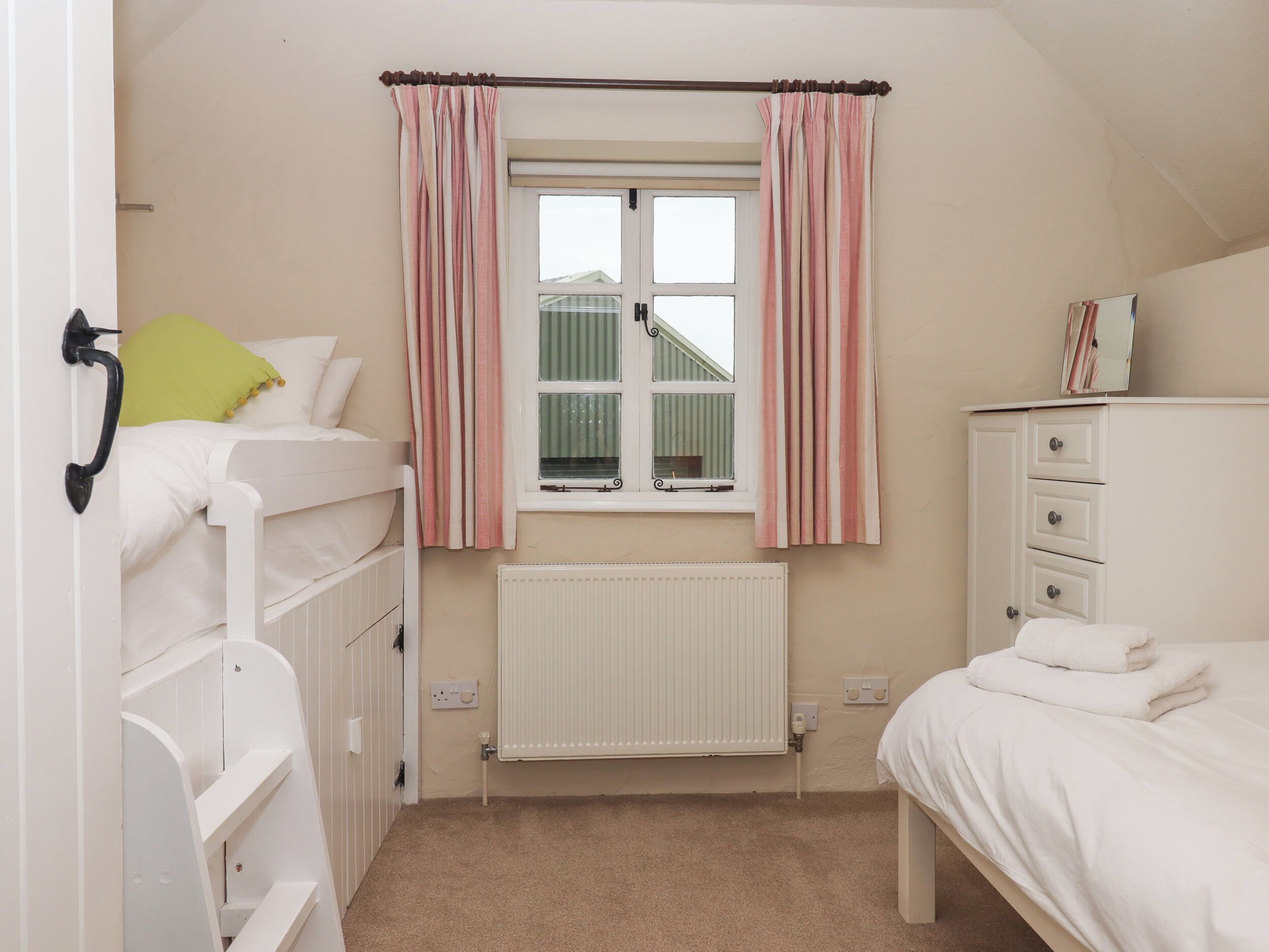 Ett sovrum med våningssängar, ett element, ett fönster med gardiner, en byrå och ett nattduksbord.
