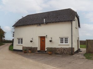 A two-story white building with a dark tiled roof, a wooden door, and two windows. There are potted plants on the ground floor. - Cherryblossom Cottage (Winkleigh)
