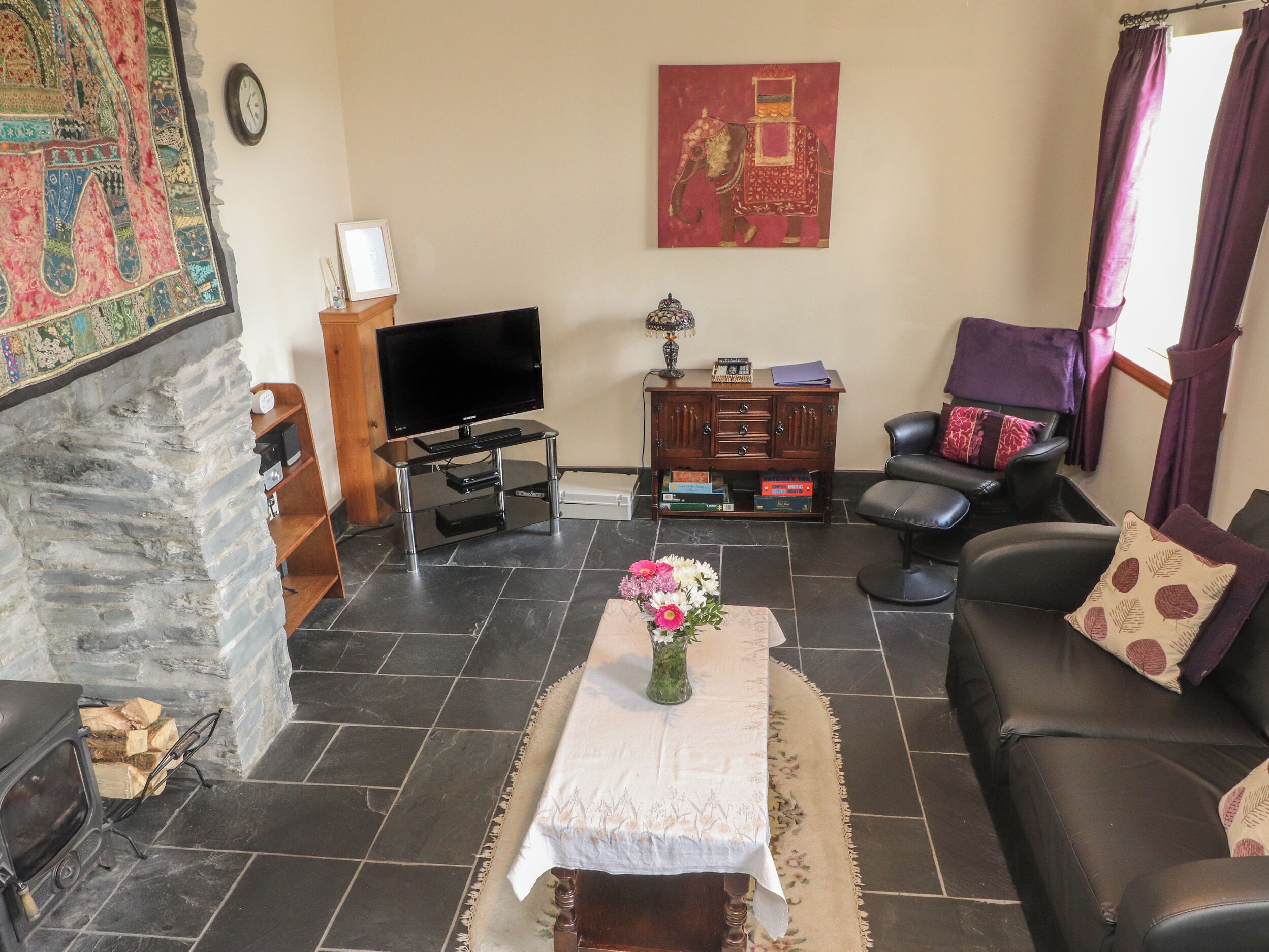 A living room with a stone fireplace, a flat-screen TV, a wooden cabinet, a sofa, and a decorative rug.
