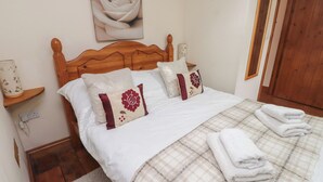 A neatly made bed with white bedding and decorative pillows, a wooden headboard, a bedside table with a lamp, and a wall-mounted picture of a rose. - Ty Llewelyn (Betws-Y-Coed)