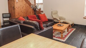 A living room with a wooden staircase, a sofa with red cushions, a beige armchair, and a wooden coffee table. - Ty Llewelyn (Betws-Y-Coed)