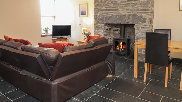 A living room with a stone fireplace, leather sofa, and a TV. - Ty Llewelyn (Betws-Y-Coed)
