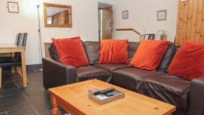 A living room with a brown leather sofa, red cushions, a wooden coffee table, and a framed picture on the wall. - Ty Llewelyn (Betws-Y-Coed)