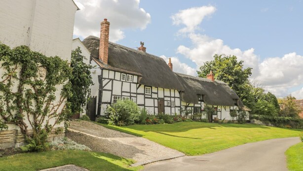 A traditional half-timbered house with a thatched roof, surrounded by a well-maintained lawn and a gravel path leading to the entrance. - Avon View (Stratford-upon-Avon)