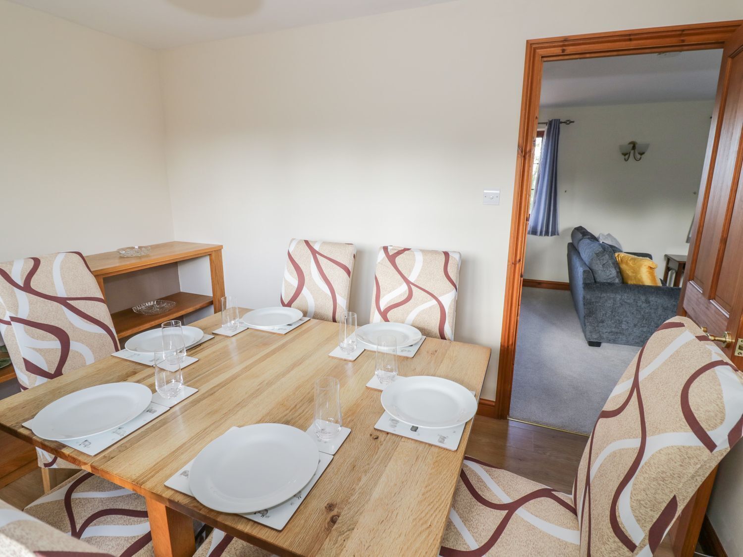 Un coin repas avec une table en bois dressée pour quatre personnes, entourée de chaises à motifs.