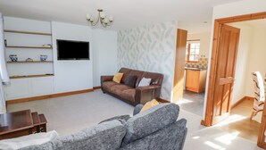 A living room with a brown leather sofa, a grey sofa, a flat-screen TV, wooden shelves, and a patterned wall. - Avon View (Stratford-upon-Avon)