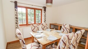 A dining area with a wooden table set for six, surrounded by patterned chairs. - Avon View (Stratford-upon-Avon)
