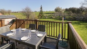 A dining area with a table set for six, surrounded by wicker chairs, overlooking a grassy landscape with trees and a fence. - Avon View (Stratford-upon-Avon)