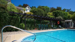 A clear blue pool with a tiled edge, surrounded by a wooden pergola and lounge chairs. - Valley View, 9 St Elmo Court (Salcombe)