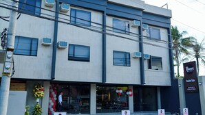 A modern hotel building with multiple air conditioning units, a sign for guests parking, and a visible entrance with a flower arrangement. - Bhive Hotel (Iloilo)
