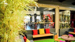 A modern indoor seating area with a green artificial turf floor, wooden benches, and colorful cushions. - Bhive Hotel (Iloilo)