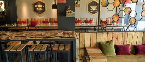 A café interior with wooden tables and benches, a hexagonal wall decoration, and a 'Benito's Café' sign.