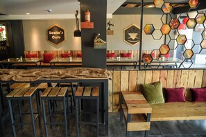 Interior de una cafetería con mesas y bancos de madera, un adorno hexagonal en la pared y un letrero que dice 'Benito's Café'.