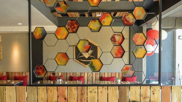 A seating area with a wooden bench, red cushions, and a hexagonal patterned wall decoration. - Bhive Hotel (Iloilo)