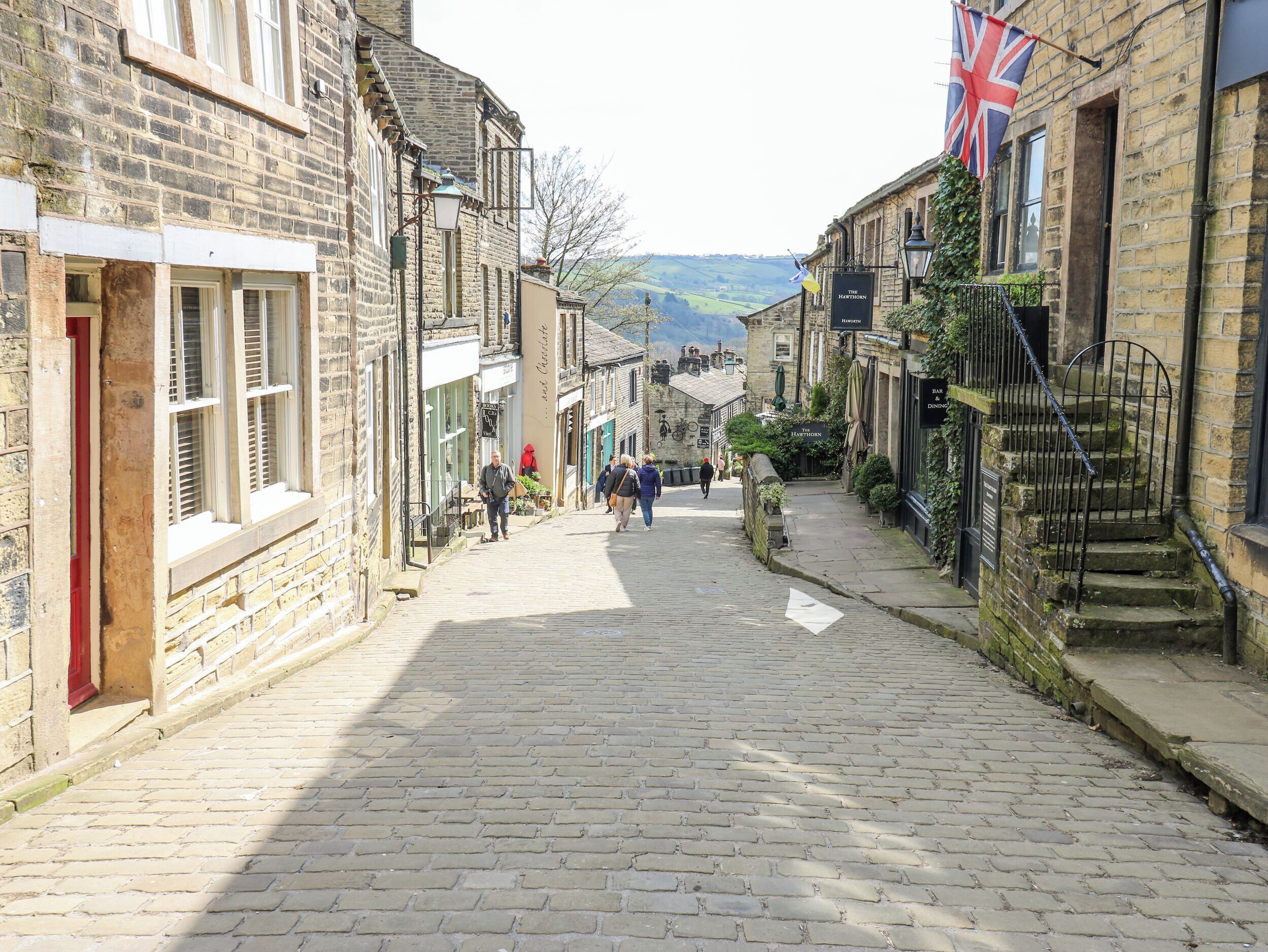 Une ruelle étroite pavée de pierres, bordée de bâtiments historiques en pierre, dont un pub appelé « The Harpstone ».