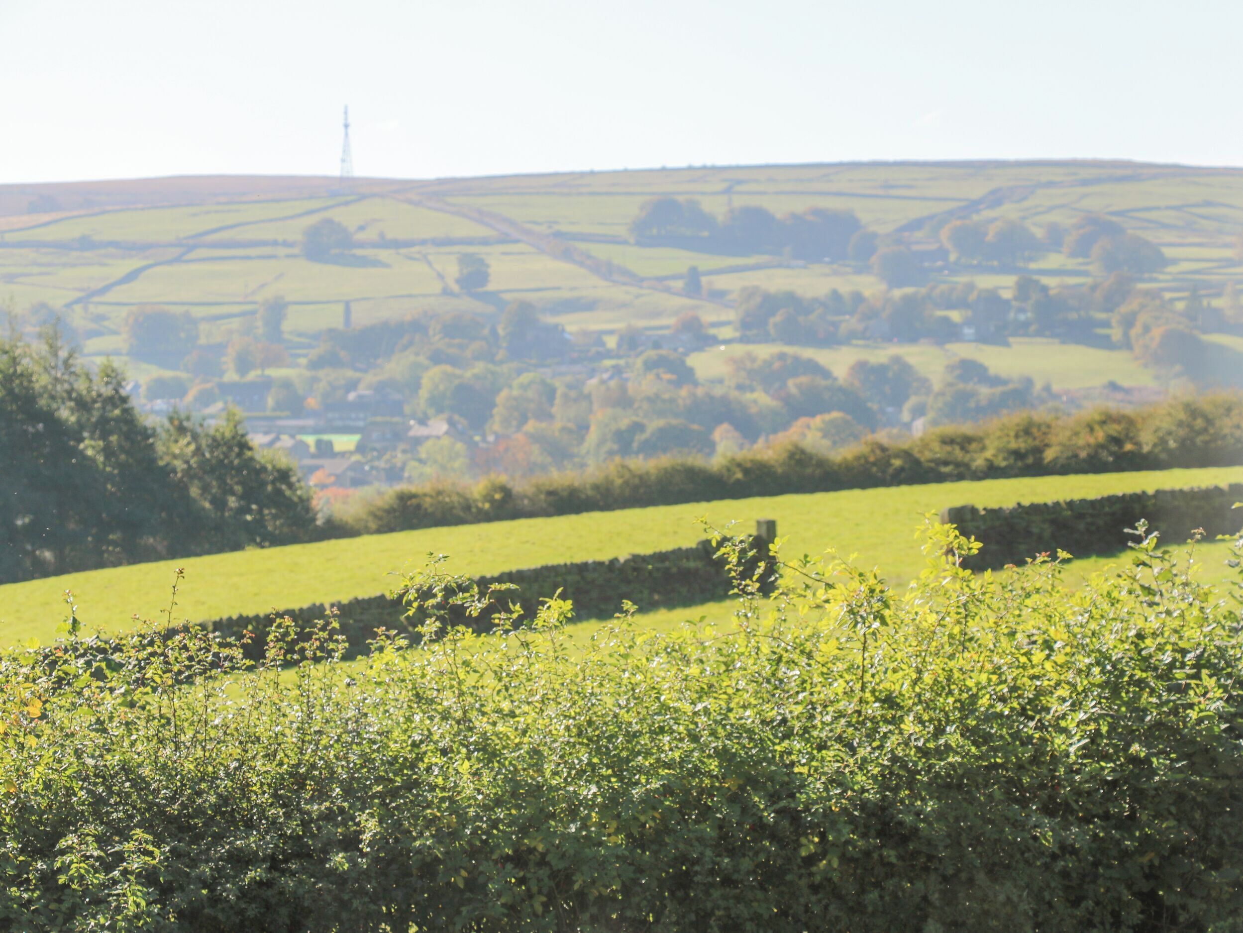 A rural landscape with rolling hills, a distant tower, and a small building in the valley.