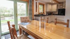 A wooden dining table with chairs, a glass vase, and a view of a river through a glass door. - Bradan Lodge (Dalmally)